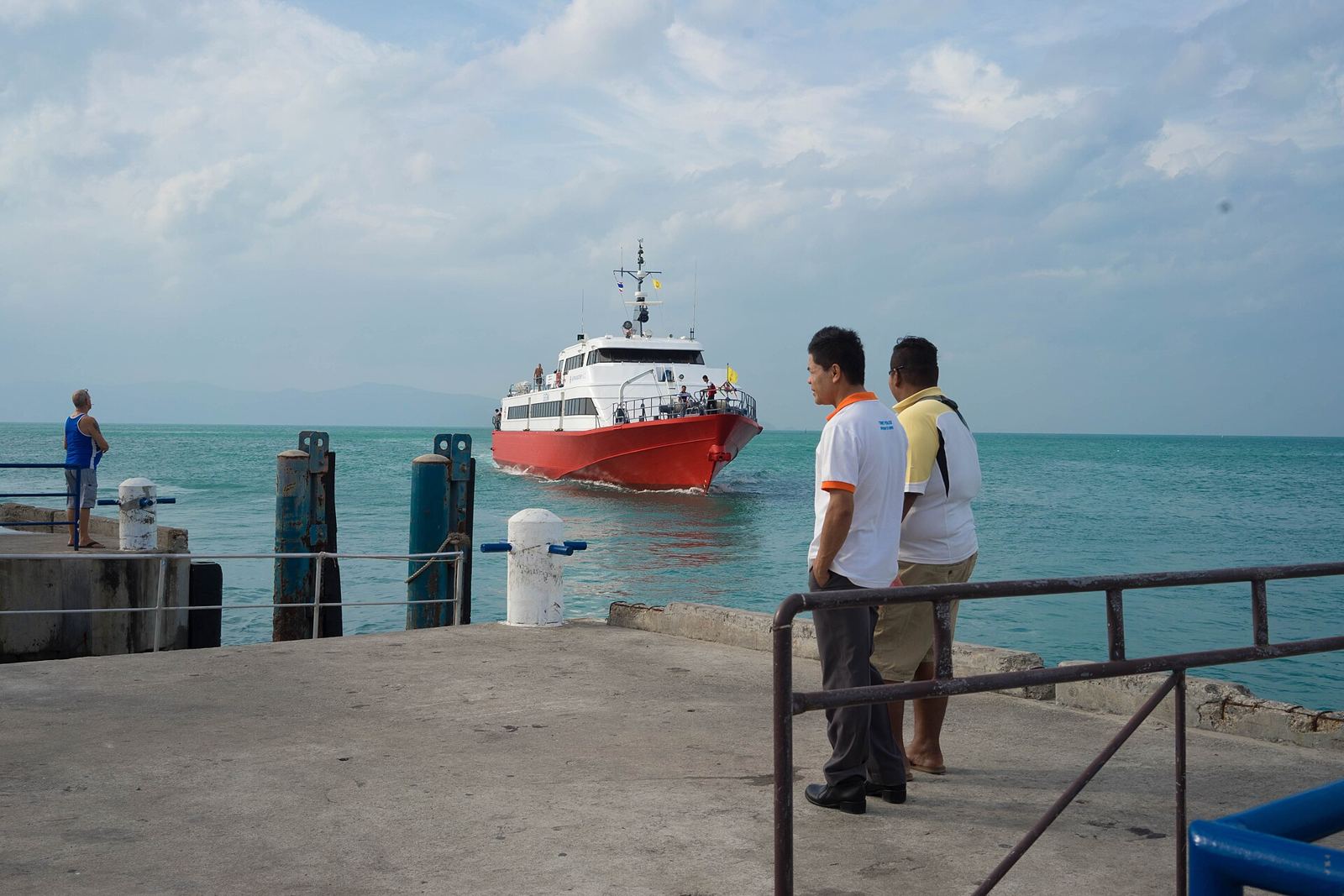 A red high-speed ferry pulling into Thong Sala Pier, Koh Phangan, as pier staff watch from the quay